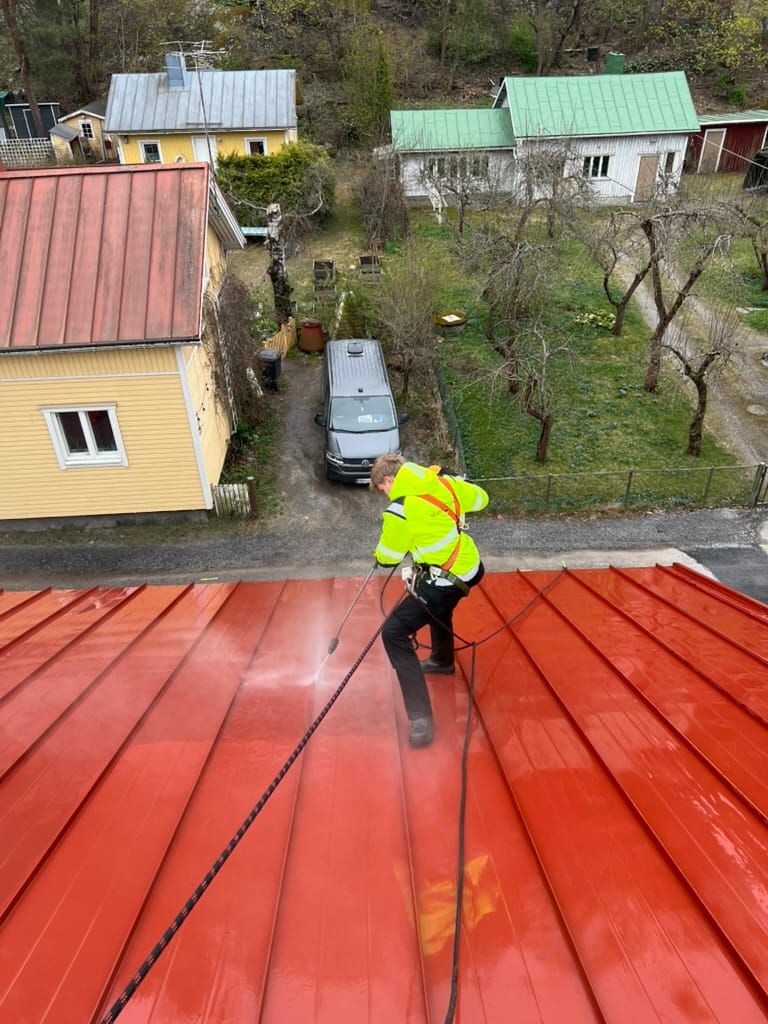 Työntekijä pesee punaista peltikattoa valjaissa